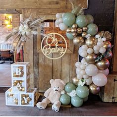 a teddy bear sitting in front of a baby sign and balloon arch with the word baby spelled out