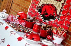 a red and white table topped with cups filled with candy next to a brick wall