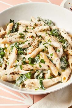 a white bowl filled with pasta and spinach covered in sauce on top of a pink table cloth