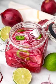 a glass jar filled with red onions and limes