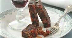 two pieces of fruit cake on a plate with a fork and wine glass in the background