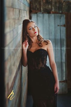 a woman in a black dress leaning against a wall