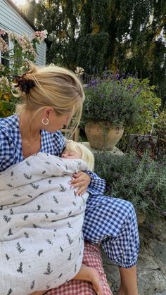 a woman is holding a baby wrapped in a blanket while she sits on the ground