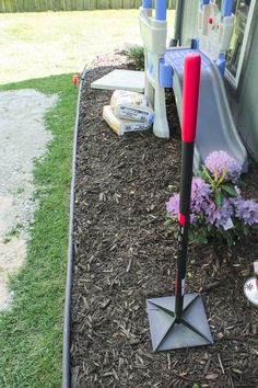 a red and black umbrella is in the mulch next to a flower bed with purple flowers