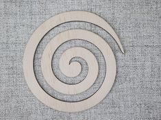 an unfinished wooden ornament that looks like a spiral on a gray fabric background