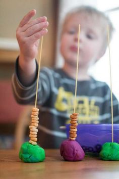 a young boy is playing with some colorful rocks and wooden skewers in front of him