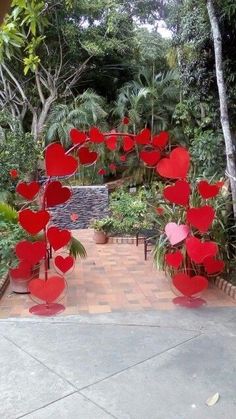 a red sculpture with hearts on it in the middle of a walkway surrounded by trees