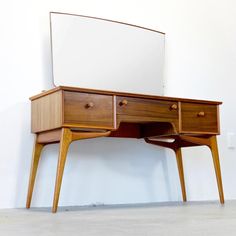 a wooden desk with two drawers and a mirror on the top, against a white wall