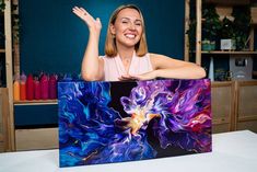 a woman is smiling and holding up a large piece of art that has been painted on it