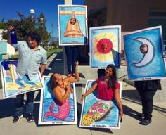 several people holding up paintings on the sidewalk