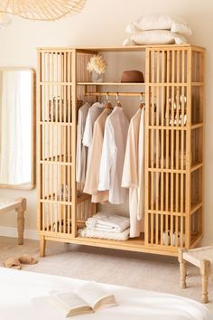 an open bamboo wardrobe with clothes hanging on the rack and a mirror in the corner