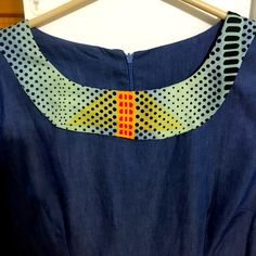 a blue dress with an orange and yellow design on the front, sitting on a hanger