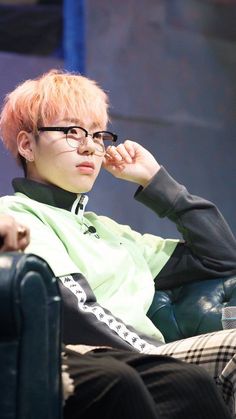 a young man with pink hair sitting in a chair and looking off to the side