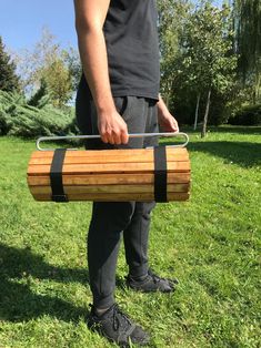 a man holding a large wooden barrel on top of a green grass covered field with trees in the background