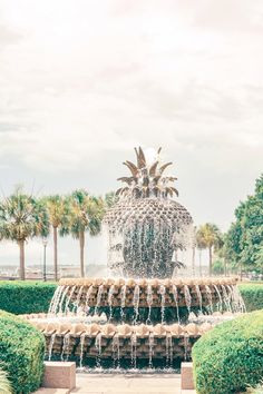 a large pineapple fountain in front of some trees and bushes with water cascading around it