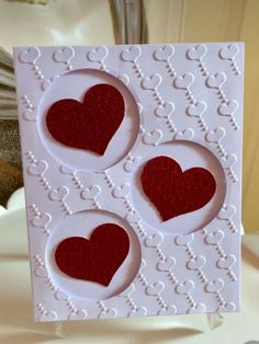 a card with three hearts on it sitting on a table next to a vase filled with flowers