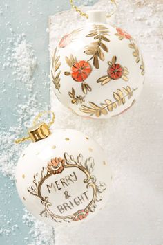 two white christmas ornaments sitting on top of a snow covered ground with the words merry and bright written in gold lettering