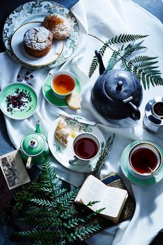 tea and pastries are on the table with green plates, cups and saucers