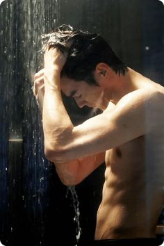 a man standing in front of a shower head with his hands on his head and arms behind his head