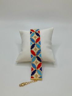 a white pillow with a colorful beaded bracelet on it and a gold chain attached to the pillow