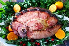 a ham is sitting on a plate surrounded by oranges and greenery as well as fresh herbs