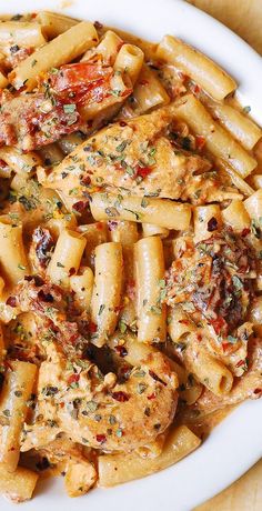 a white plate topped with pasta and chicken covered in sauce on top of a wooden table