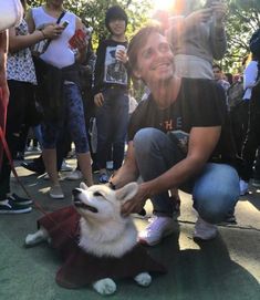 a person kneeling down petting a dog on a leash with people in the background