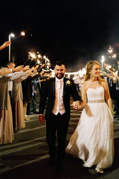 a newly married couple holding hands as they walk through the street with sparklers