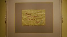 a piece of yellow paper with writing on it hanging in a white framed frame against a wall