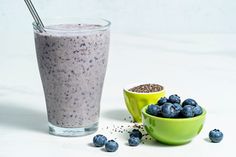 a green bowl filled with blueberries next to a drink