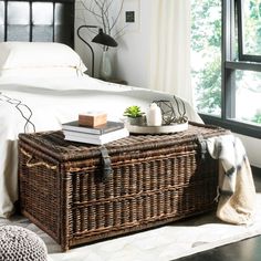 a wicker trunk sitting on top of a bed next to a night stand and window