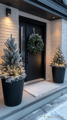 two potted christmas trees sitting on the front step of a house with lights around them