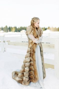 a woman standing in the snow wearing a long fur coat and holding her arms crossed