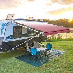 an rv parked on the grass with a table and chairs in front of it at sunset