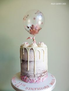 a birthday cake with white frosting and pink sprinkles on top, topped with a large balloon