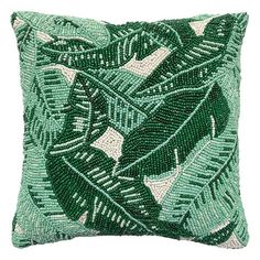 a green and white beaded pillow with leaves on the front, sitting on a white surface