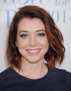 a smiling woman with red hair and blue eyeshade, wearing a black top