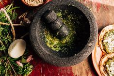 an old mortar bowl with pest on it next to some herbs and garlic in bowls