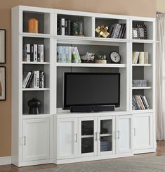 a white entertainment center with bookshelves and a flat screen tv mounted on the wall