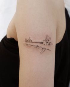 a woman's arm with a small tattoo of a barn and trees on it