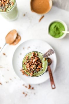 two glasses filled with green smoothie on top of a white plate next to spoons