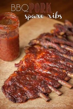 bbq pork spare ribs on a cutting board next to a jar of barbecue sauce