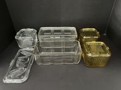 three clear plastic containers and one yellow glass container are sitting side by side on a black surface