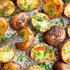 baked potatoes with parmesan cheese and herbs on a sheet of parchment paper next to a fork