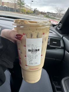 a person holding up a cup of coffee in their car