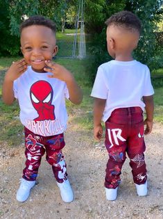 two young boys standing next to each other in front of trees and grass, both wearing spiderman t - shirts