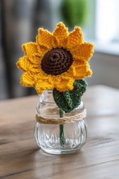 a crocheted sunflower in a small glass jar on a wooden table top