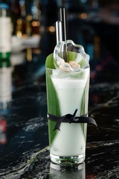 a tall glass filled with milk and green leafy garnish on top of a table