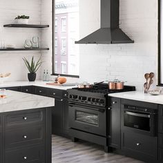 a kitchen with an oven, stove and counter tops in black painted wooden cabinets next to a white brick wall