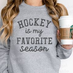 a woman holding a cup of coffee and wearing a sweatshirt that says hockey is my favorite season